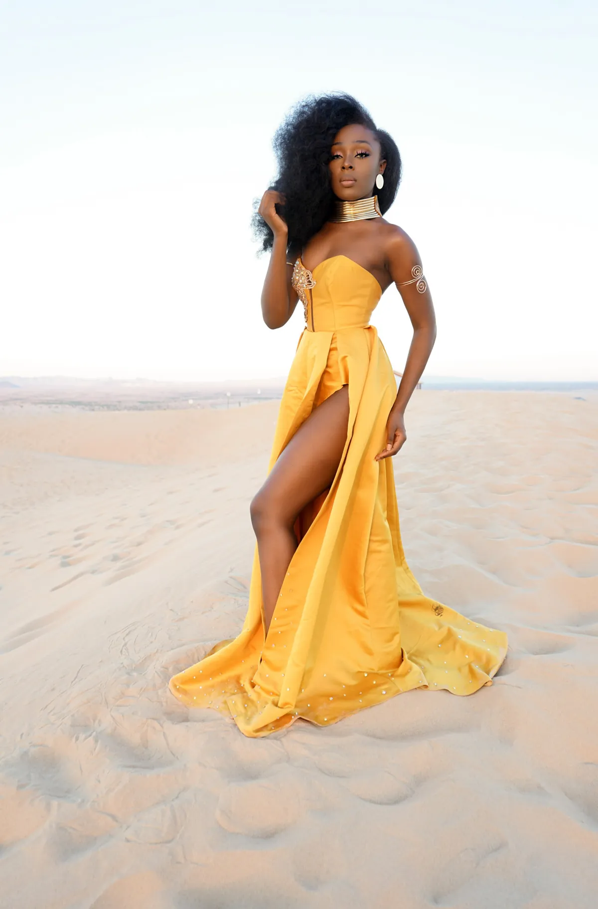 Model in a flowing yellow gown posing on sand dunes