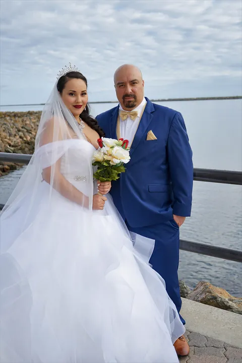 Bride and groom in a blue suit standing together by the water